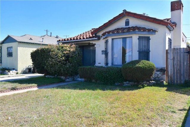 mediterranean / spanish-style home with a tile roof, a chimney, fence, a front lawn, and stucco siding