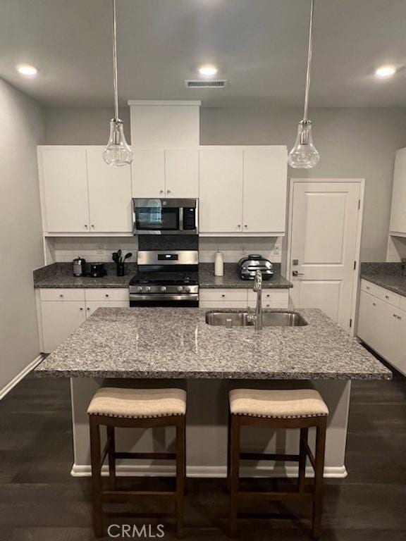 kitchen with hanging light fixtures, backsplash, appliances with stainless steel finishes, a kitchen island with sink, and a sink