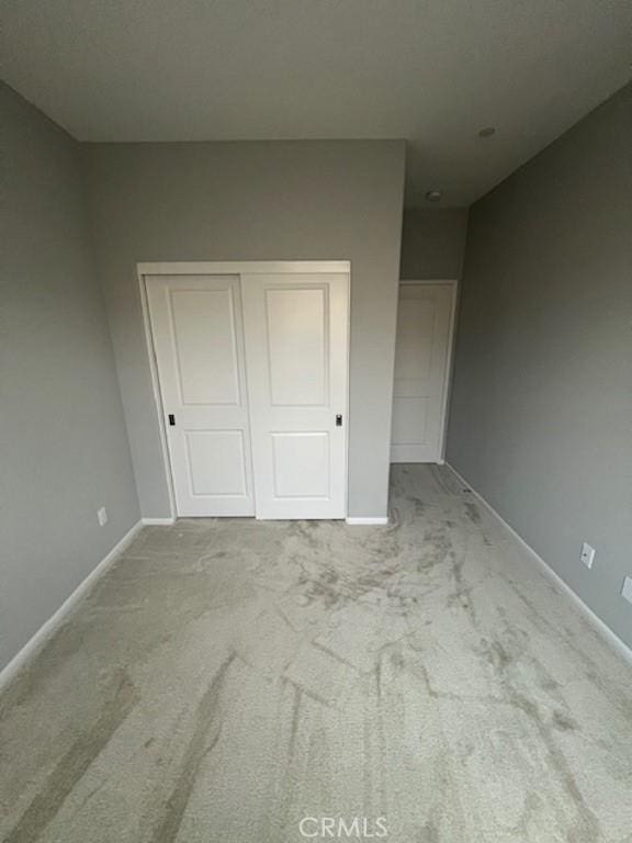 unfurnished bedroom with a closet, light carpet, and baseboards