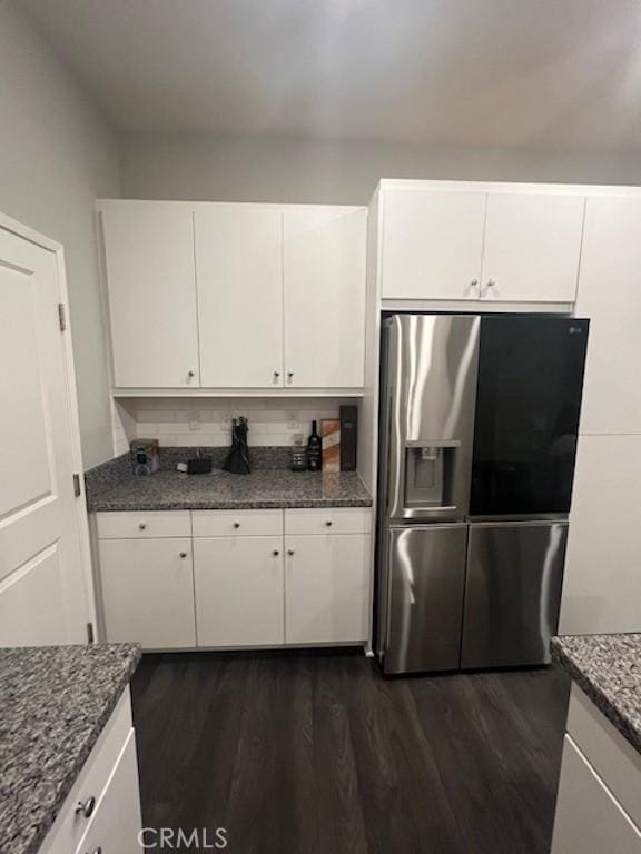 kitchen featuring stainless steel fridge, decorative backsplash, dark wood-style floors, dark stone countertops, and white cabinetry