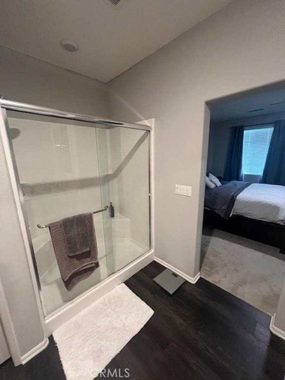 ensuite bathroom featuring a stall shower, ensuite bath, baseboards, and wood finished floors