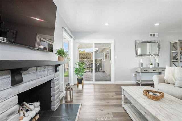 living area with recessed lighting, visible vents, a brick fireplace, wood finished floors, and baseboards