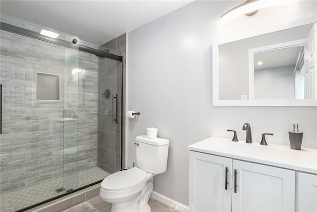 full bathroom with toilet, a stall shower, baseboards, and vanity
