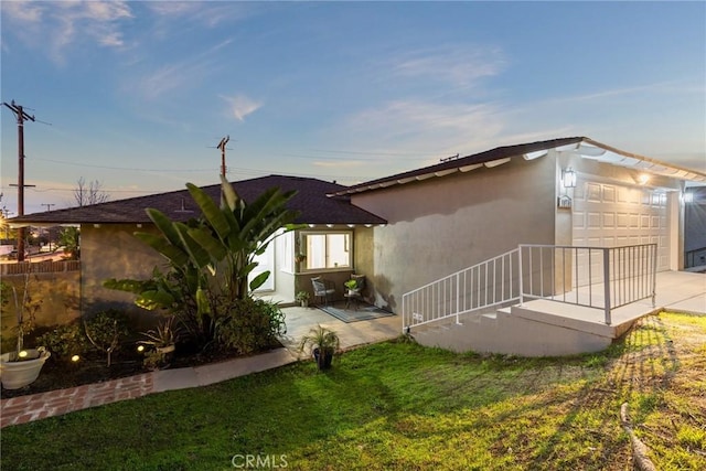 back of property at dusk with a garage, stucco siding, a patio, and a yard