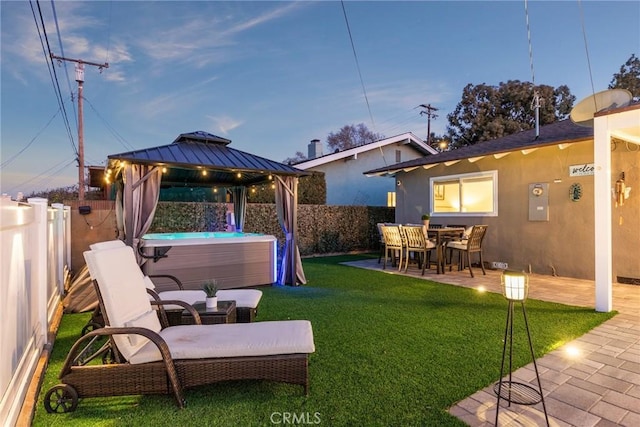 yard at dusk featuring a patio area, a hot tub, a gazebo, and a fenced backyard