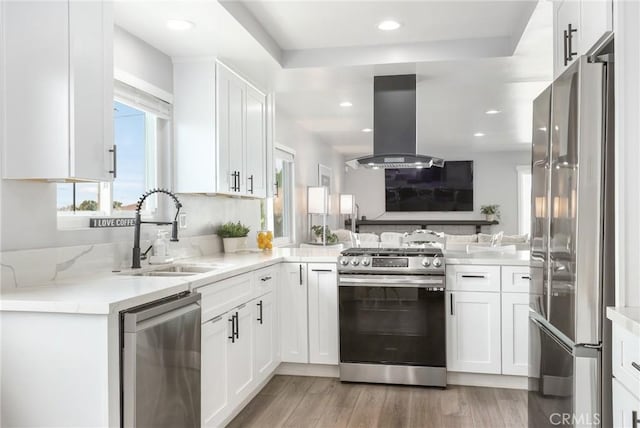 kitchen featuring island range hood, appliances with stainless steel finishes, light stone countertops, white cabinetry, and a sink