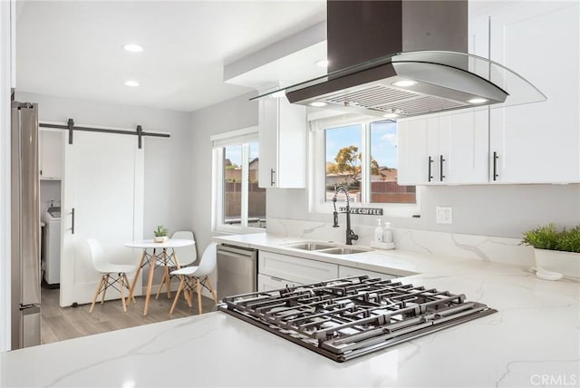 kitchen featuring light stone counters, island exhaust hood, stainless steel appliances, a barn door, and a sink