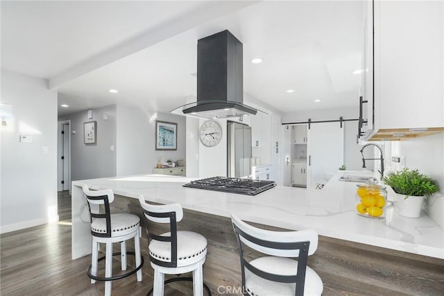 kitchen with a barn door, white cabinetry, a sink, island range hood, and a peninsula