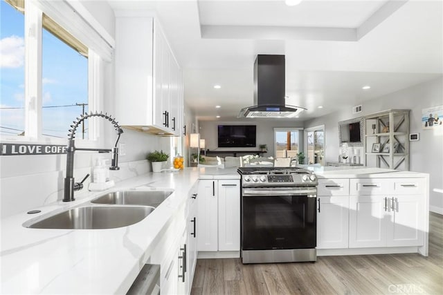 kitchen with open floor plan, gas stove, island exhaust hood, and white cabinetry