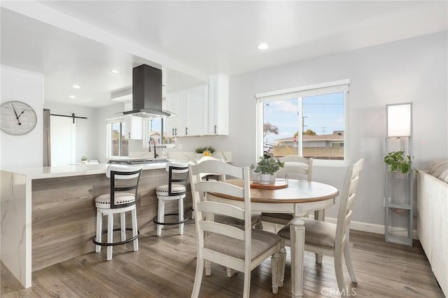 dining area with light wood-type flooring, baseboards, recessed lighting, and a barn door