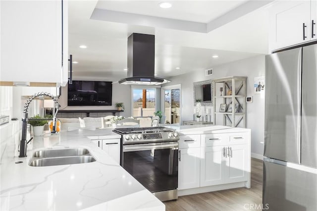 kitchen with stainless steel appliances, open floor plan, white cabinets, a sink, and island range hood