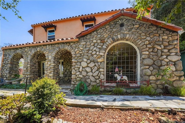 view of front of home with a tiled roof, stone siding, and stucco siding