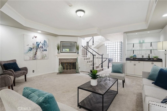 living room with light carpet, ornamental molding, stairway, a tray ceiling, and a glass covered fireplace