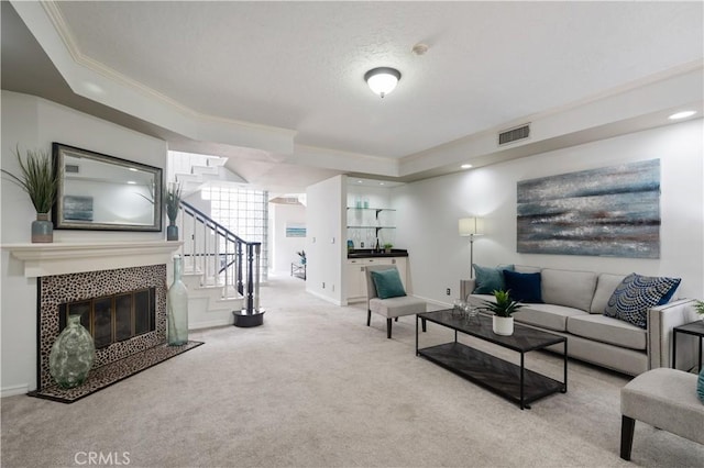 living room featuring light carpet, visible vents, a tiled fireplace, ornamental molding, and stairs