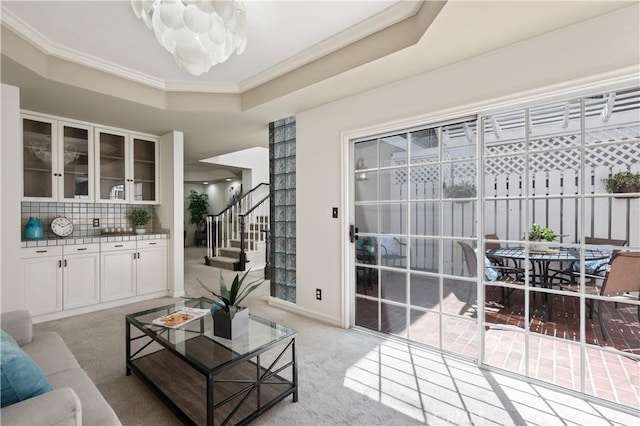 living room featuring light carpet, baseboards, a raised ceiling, stairway, and crown molding