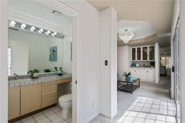 bathroom featuring a tray ceiling, backsplash, toilet, ornamental molding, and vanity