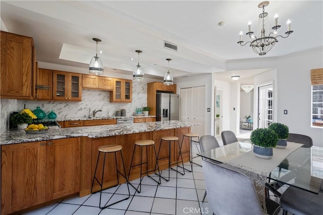 kitchen with light stone counters, hanging light fixtures, appliances with stainless steel finishes, a raised ceiling, and glass insert cabinets