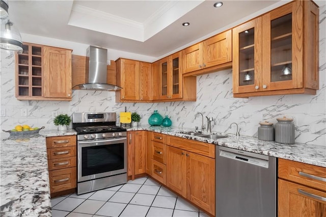 kitchen featuring a raised ceiling, appliances with stainless steel finishes, glass insert cabinets, wall chimney range hood, and light stone countertops