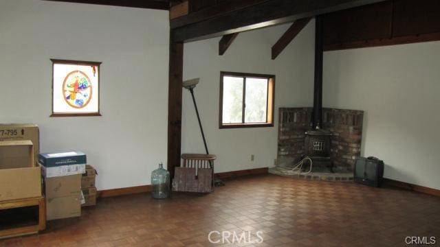 living area featuring a wood stove, lofted ceiling with beams, and baseboards