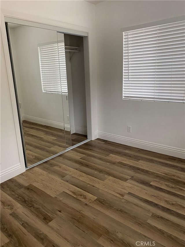 unfurnished bedroom with baseboards, dark wood-style flooring, and a closet