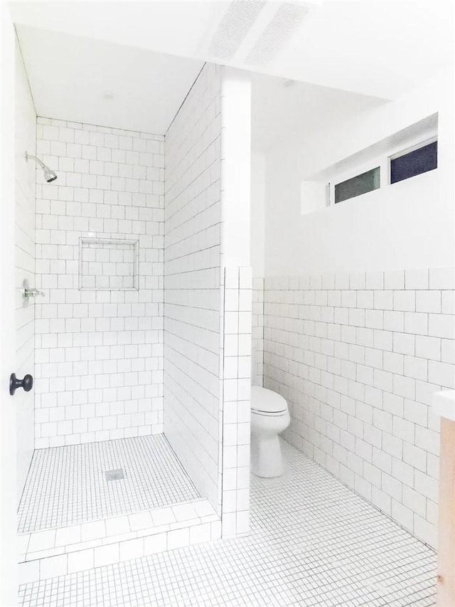 full bathroom featuring a stall shower, wainscoting, toilet, tile patterned flooring, and tile walls