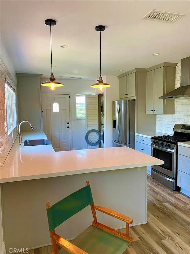 kitchen featuring light wood-style flooring, stainless steel appliances, stacked washer / dryer, visible vents, and light countertops