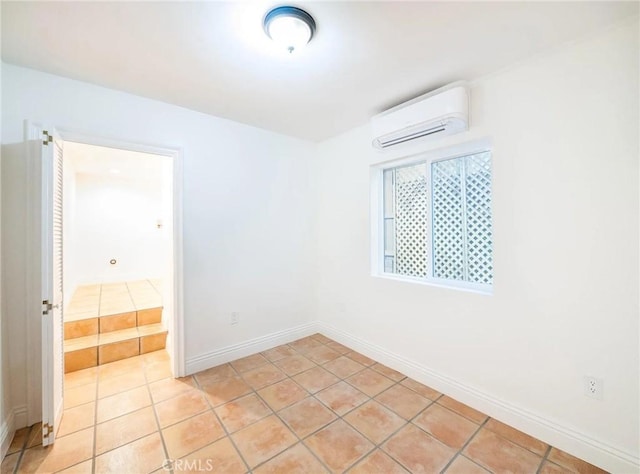 empty room with a wall mounted air conditioner, baseboards, and light tile patterned floors