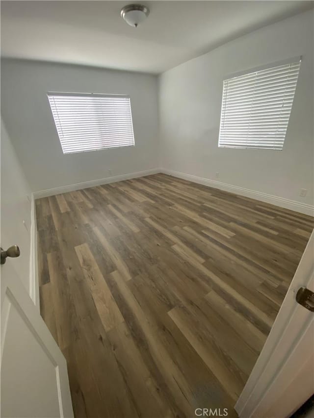 spare room featuring dark wood-style flooring and baseboards