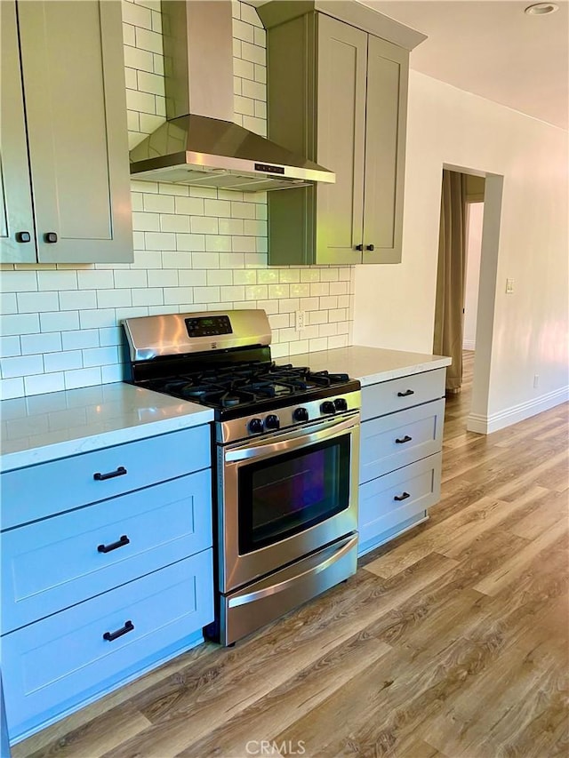 kitchen featuring light countertops, wall chimney range hood, stainless steel gas range, and light wood-type flooring