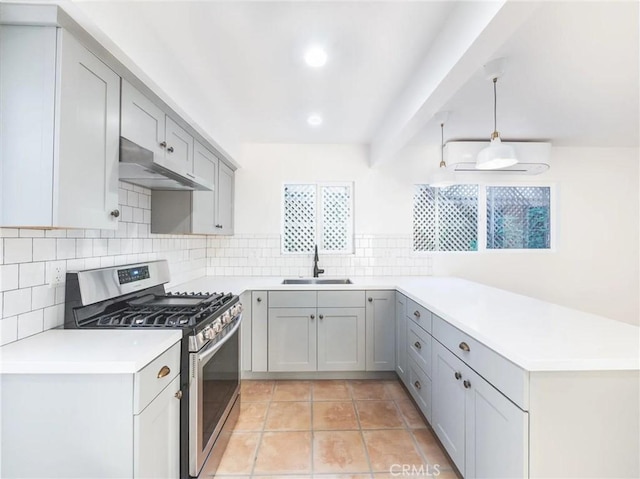 kitchen with pendant lighting, light countertops, a sink, stainless steel gas range, and under cabinet range hood