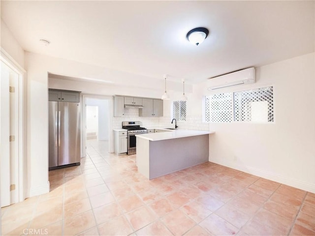 kitchen with light countertops, a wall mounted AC, appliances with stainless steel finishes, a peninsula, and under cabinet range hood