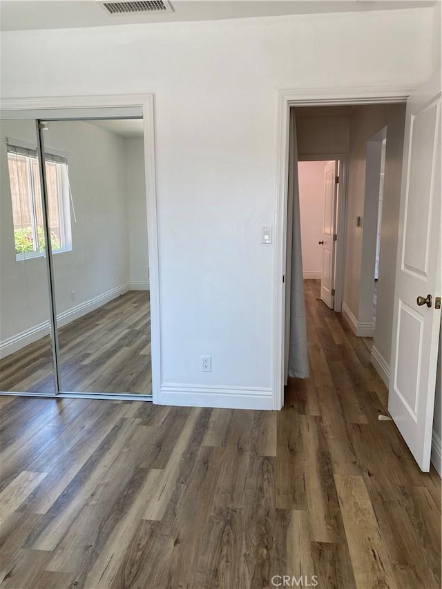 unfurnished bedroom featuring dark wood-type flooring, a closet, visible vents, and baseboards