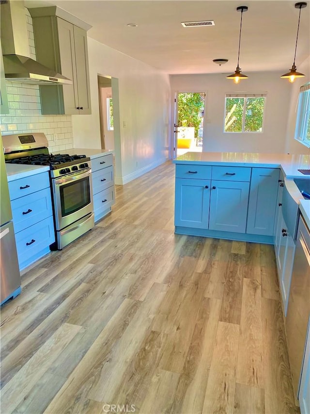 kitchen with decorative light fixtures, light countertops, stainless steel gas range oven, and wall chimney range hood