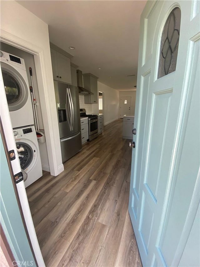 kitchen featuring stacked washer / dryer, dark wood-style floors, stainless steel appliances, gray cabinetry, and wall chimney range hood