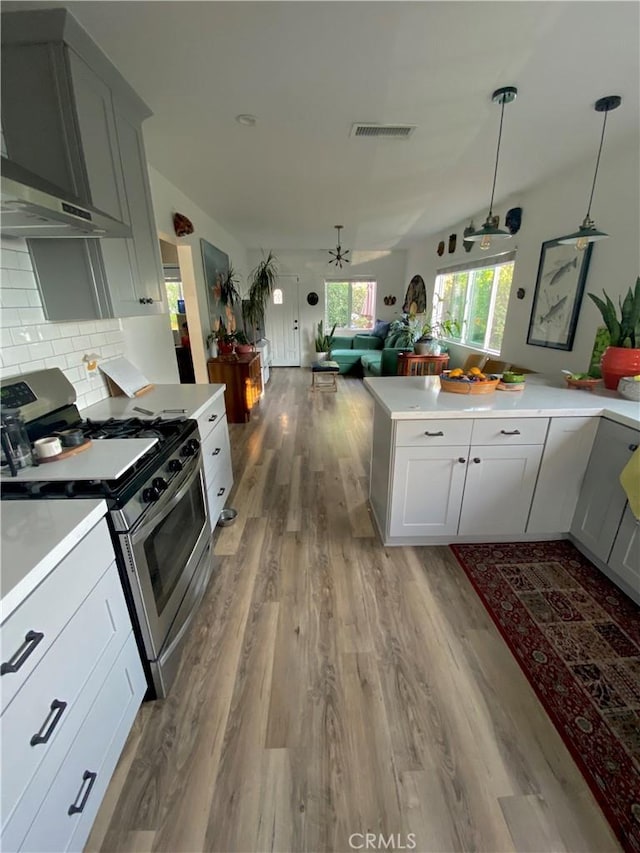 kitchen featuring visible vents, open floor plan, light countertops, wall chimney range hood, and stainless steel gas range