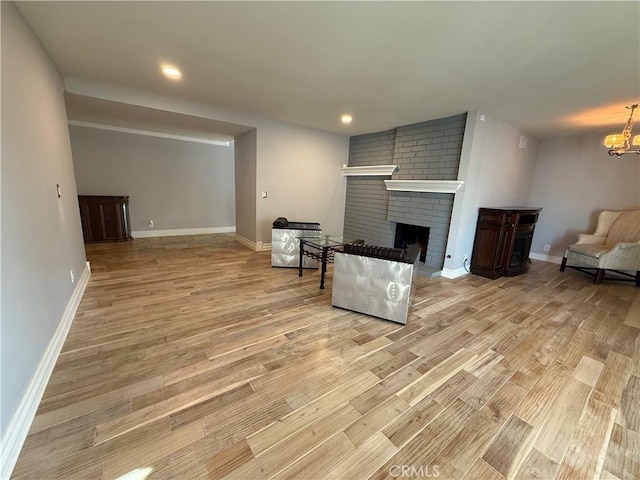 living room with light wood-style floors, a fireplace, baseboards, and an inviting chandelier