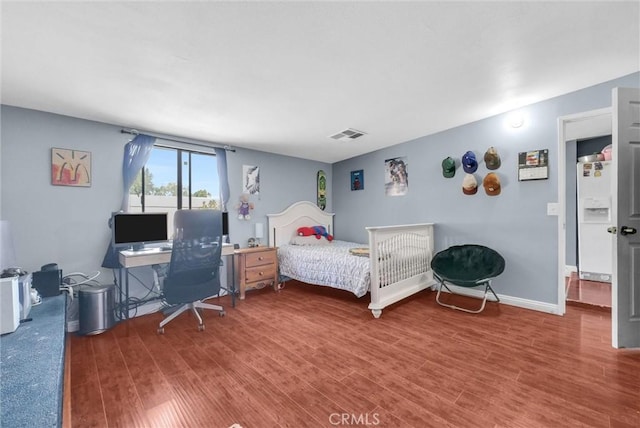 bedroom with white refrigerator with ice dispenser, visible vents, baseboards, and wood finished floors