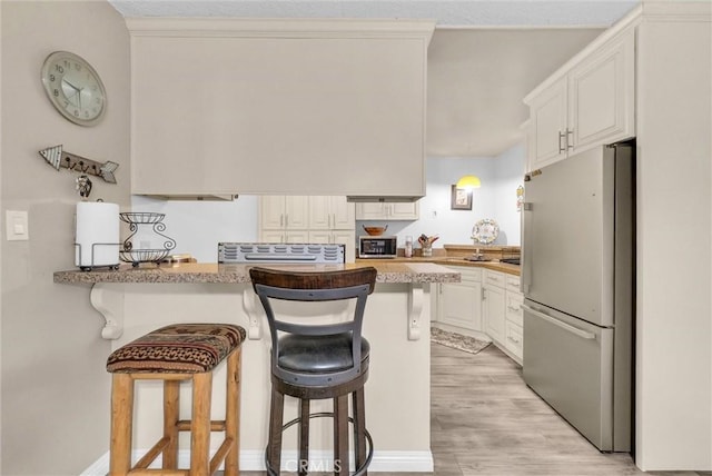 kitchen with a peninsula, white cabinetry, stainless steel refrigerator, and a kitchen breakfast bar