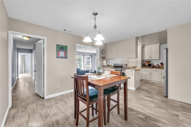 dining room featuring light wood-style flooring, visible vents, and baseboards