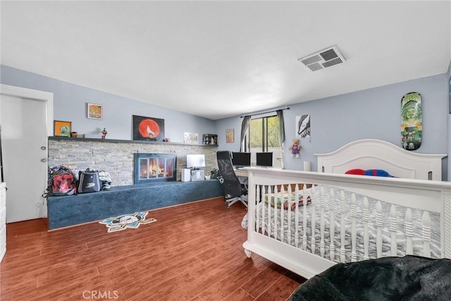 bedroom featuring a glass covered fireplace, visible vents, and wood finished floors