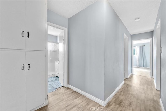 hallway with baseboards, a wealth of natural light, and light wood-style floors