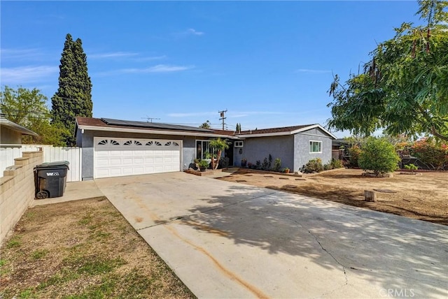 single story home with a garage, fence, driveway, roof mounted solar panels, and stucco siding