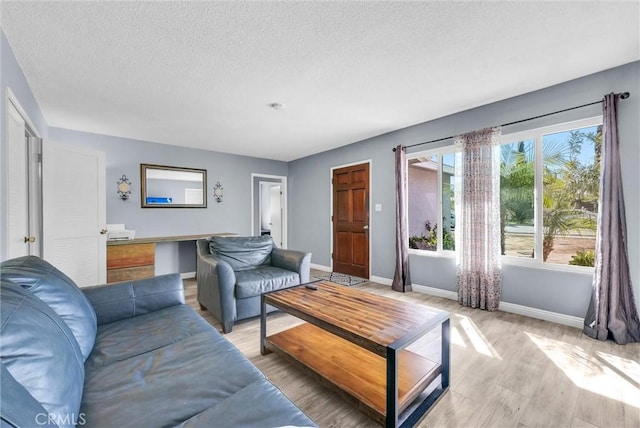 living area with baseboards, a textured ceiling, and light wood finished floors