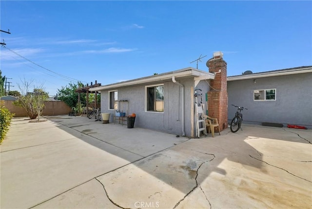 rear view of house with a chimney, fence, a patio, and stucco siding