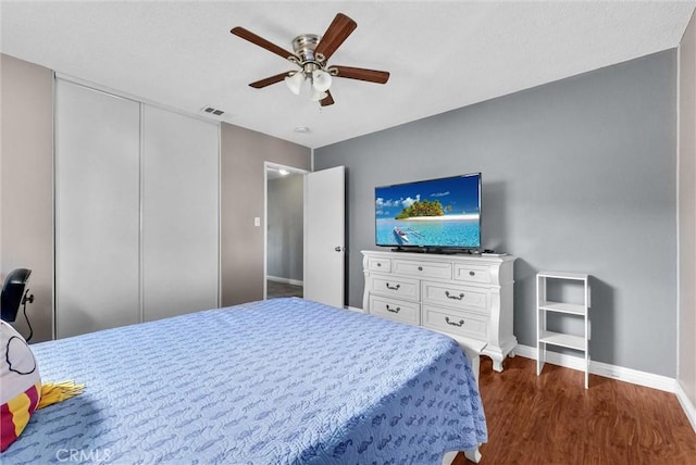 bedroom with visible vents, baseboards, a ceiling fan, dark wood-type flooring, and a closet