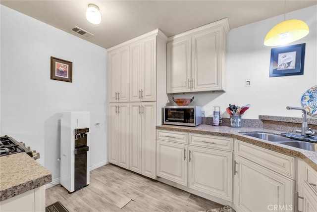 kitchen with a sink, visible vents, white cabinetry, hanging light fixtures, and stainless steel microwave