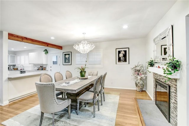 dining area featuring light wood-style flooring, a fireplace, baseboards, and beamed ceiling