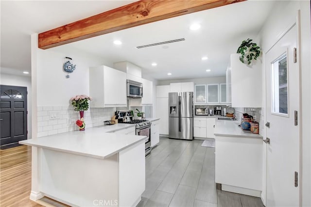 kitchen with light countertops, appliances with stainless steel finishes, glass insert cabinets, white cabinetry, and a peninsula