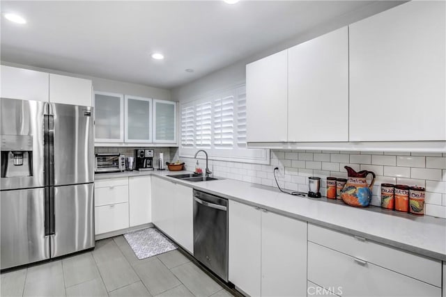 kitchen featuring glass insert cabinets, stainless steel appliances, light countertops, white cabinetry, and a sink