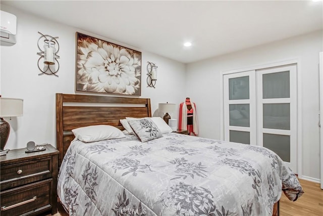 bedroom featuring a wall unit AC, light wood-style flooring, and recessed lighting